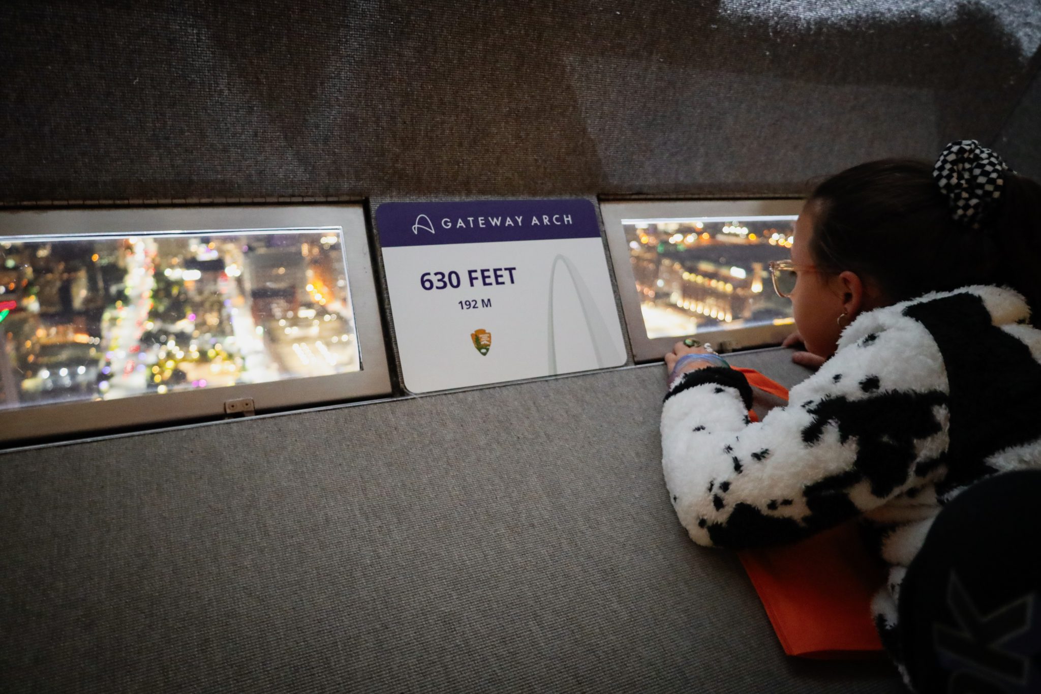 A young girl dressed in a Halloween costume looks out a window at the top of the Gateway Arch.