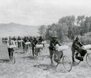 Historic black and white photo of the Iron Riders traveling across an open field. Image provided by National Park Service.