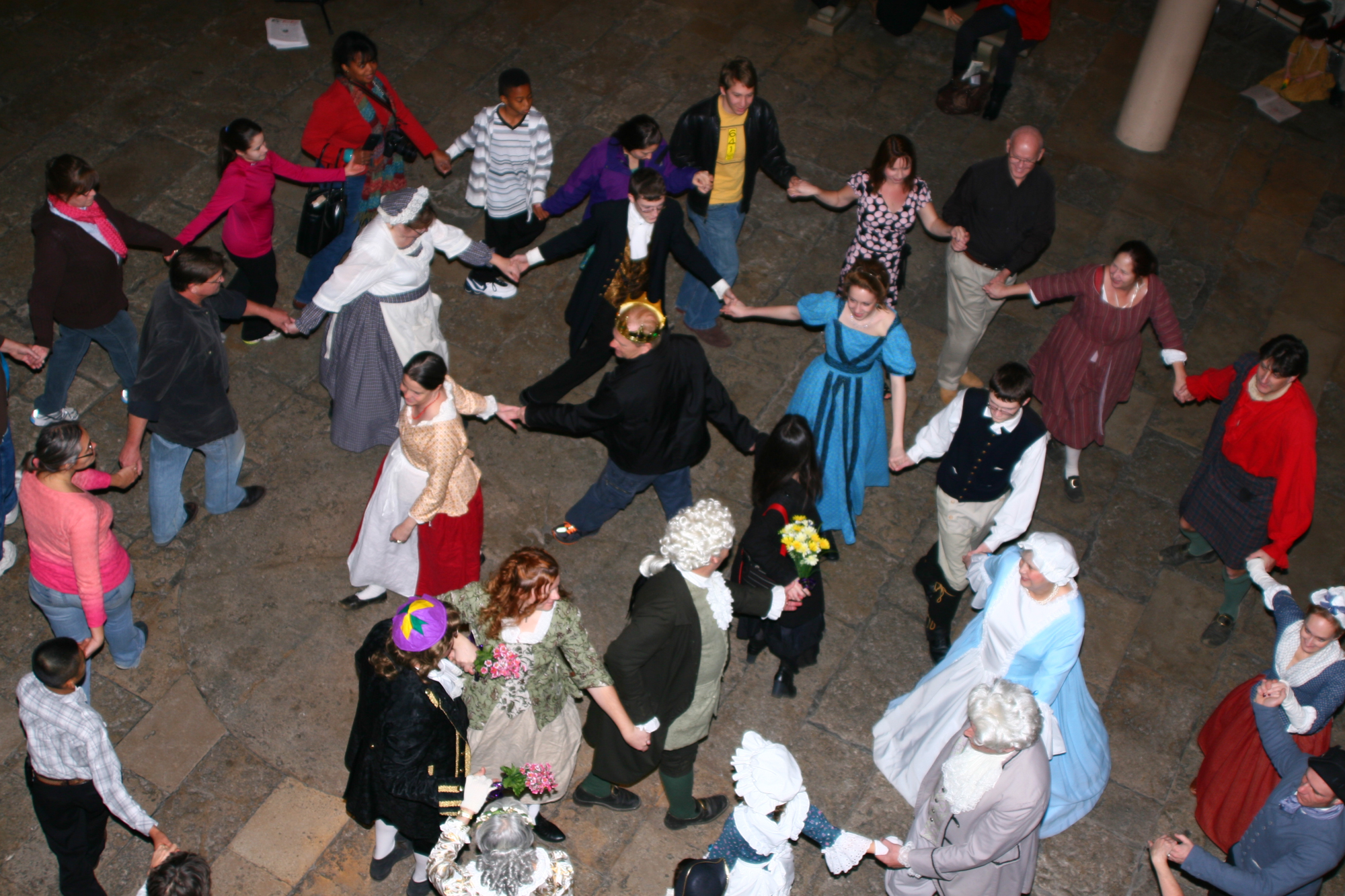 A few dozen people dance while holding hands, some dressed in Victorian formal wear, during the Twelfth Afternoon Ball event at the Gateway Arch.