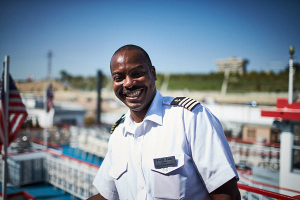 riverboat captain standing on the top deck of the boat smiling.